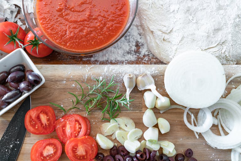 A flat lay of fresh tomatoes, garlic, onions, and herbs ready for making a homemade pizza sauce.