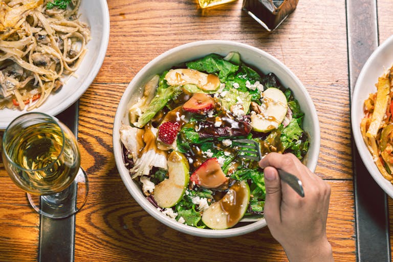 An inviting meal featuring a bowl of fresh salad with fruits and pasta, paired with a glass of white wine.