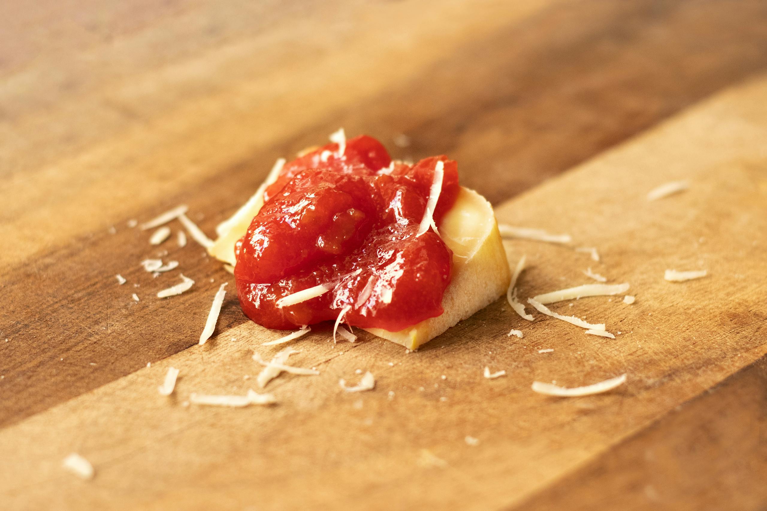 Close-up of grated parmesan and tomato sauce on a rustic wooden board, showcasing an authentic culinary presentation.