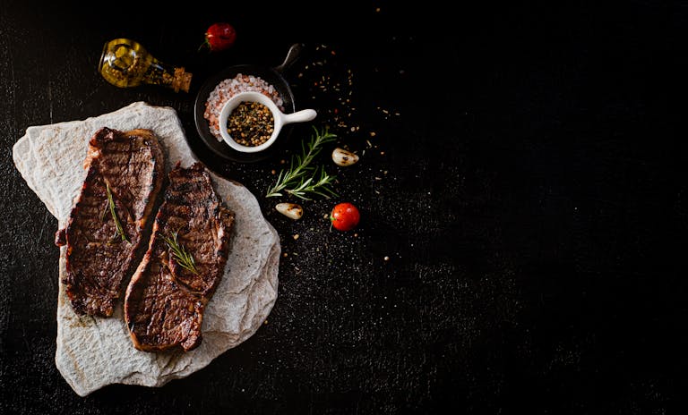 Delicious grilled steak served with rosemary, garlic, and spices on a stone slab, perfect for a gourmet meal.