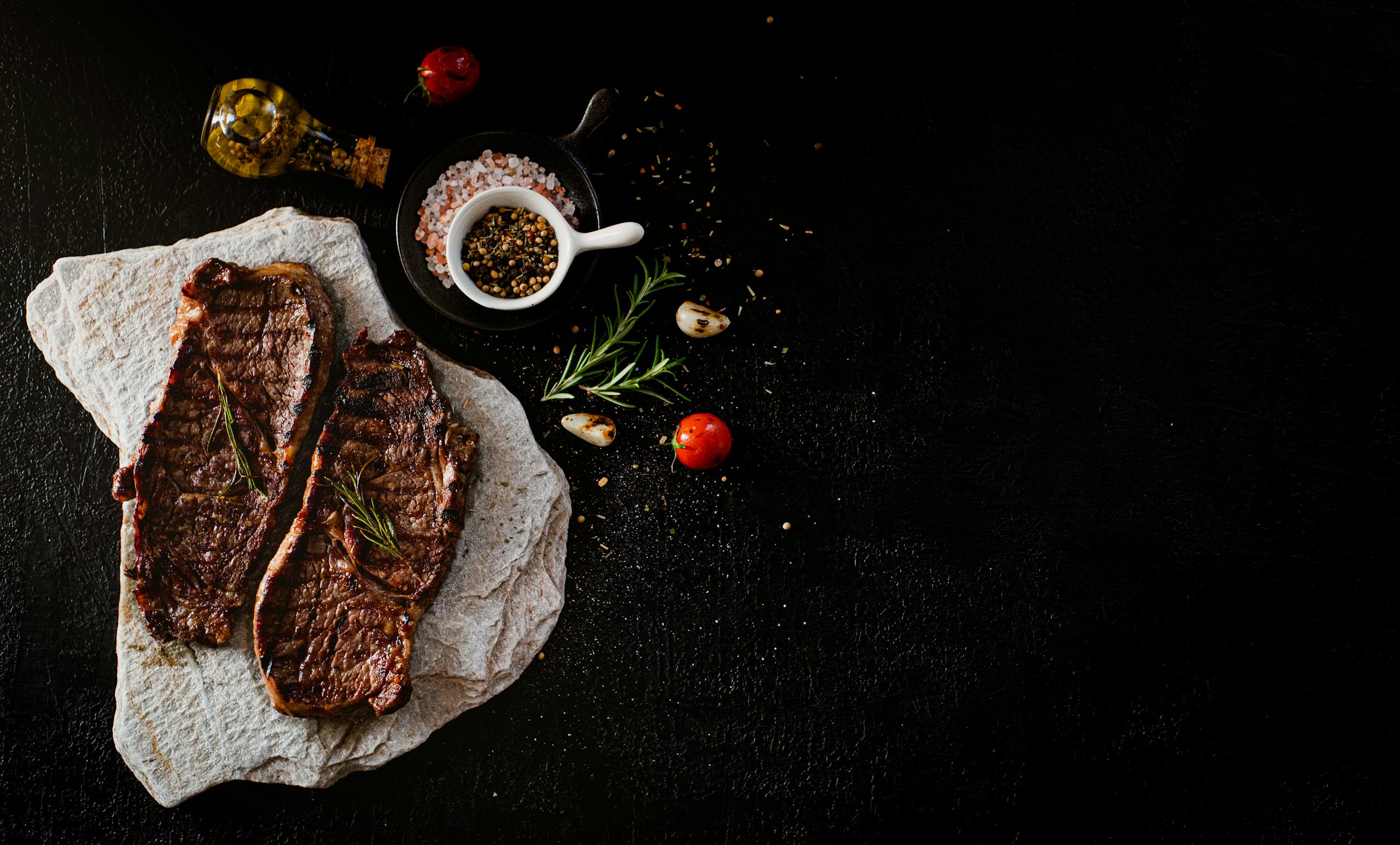 Delicious grilled steak served with rosemary, garlic, and spices on a stone slab, perfect for a gourmet meal.