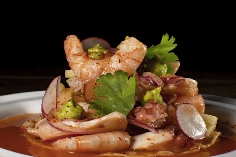 Delicious seafood platter featuring shrimp and octopus with spicy sauce and garnishes.