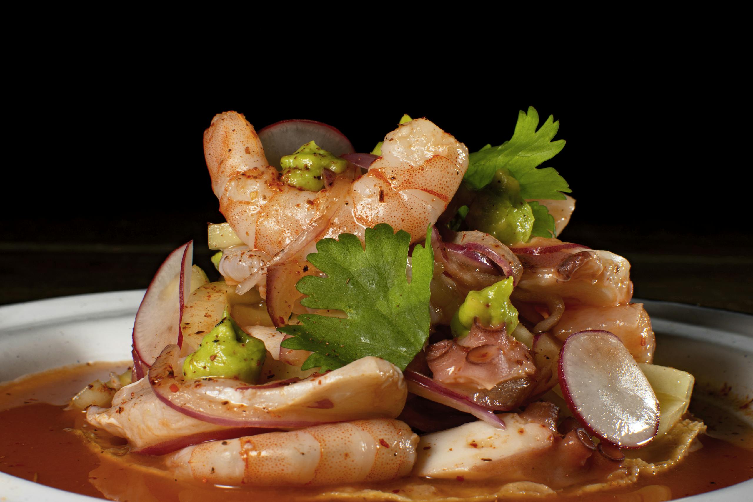 Delicious seafood platter featuring shrimp and octopus with spicy sauce and garnishes.