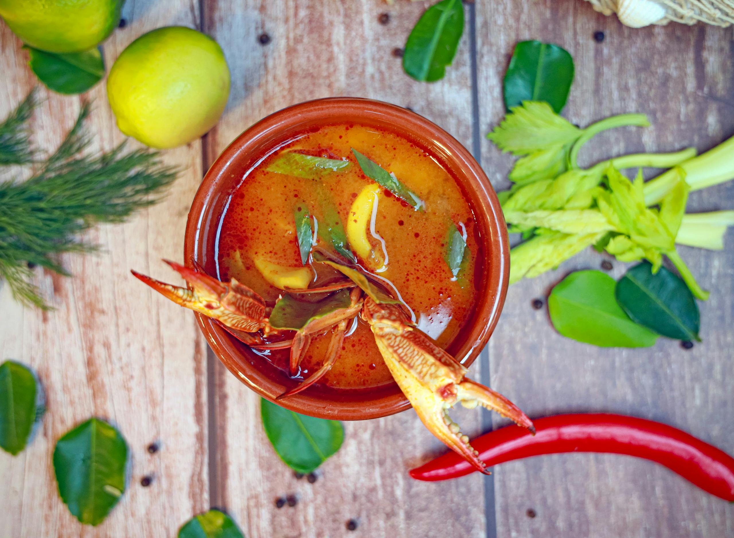Delicious spicy crab soup garnished with fresh herbs, lemon, and chili peppers.