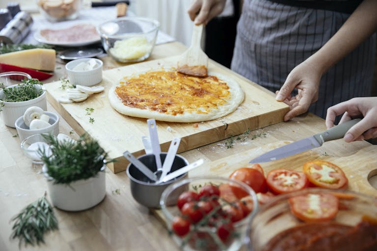 Hands crafting a delicious homemade pizza with fresh ingredients on a wooden board.